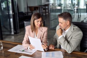 A lawyer and their client sit next to each other at a table, and the lawyer has a piece of paper in their hand and discusses with their client if an employer can withhold commission if this individual quits.