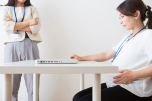 A pregnant employee sits at a table with a laptop while her boss looks on. A lawyer can advise you of the protections offered under the Pregnant Workers Fairness Act (PWFA) and if it covers your case.