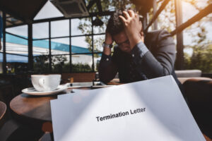 A man holds his head in his hands as someone hands him a termination letter. An employment lawyer can advise on how to build a strong wrongful termination case.